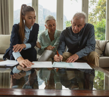 Active senior couple signing agreement with real estate agent documents living room 360x320