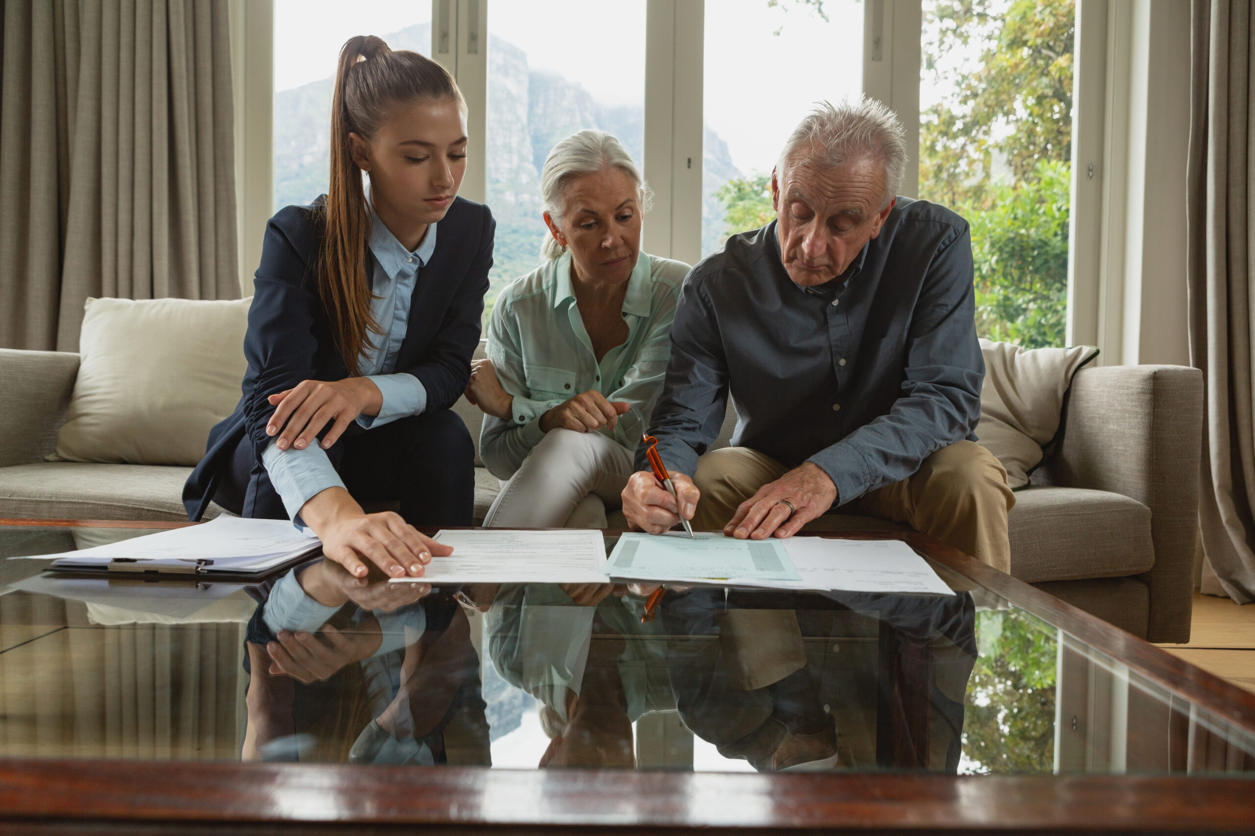 Active senior couple signing agreement with real estate agent documents living room scaled